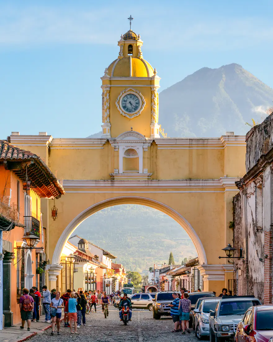The yellow Santa Catalina Arch in Antigua Guatemala with a volcano behind